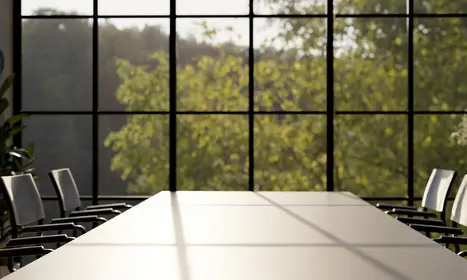 A modern meeting room features a large meeting table and large window with a green mountain view.